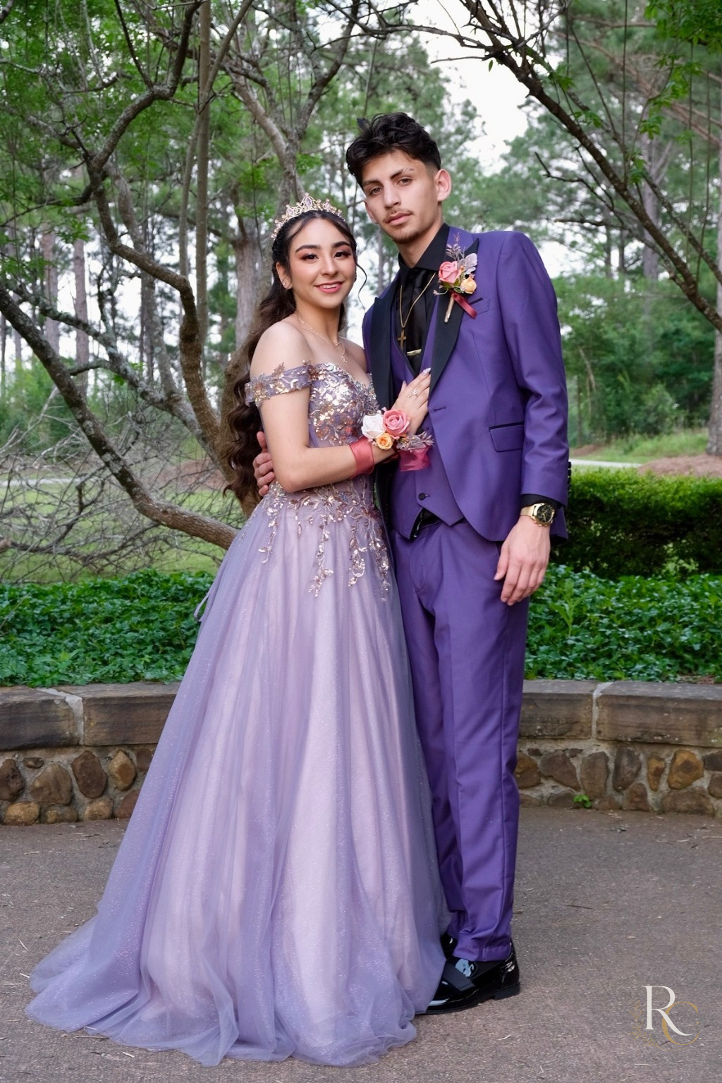 A couple in purple formalwear standing together beneath trees